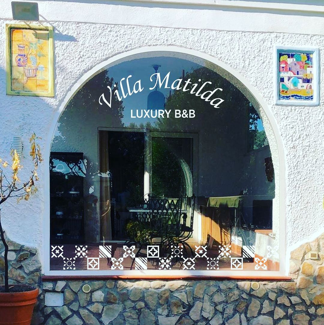 The charming entrance of Villa Matilde Luxury B&B features a distinctive arched doorway with decorative tilework and colorful artwork on the whitewashed facade.