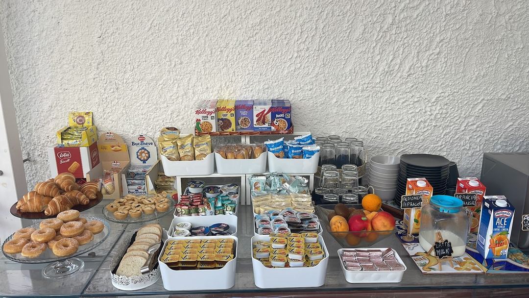 An abundant breakfast buffet display featuring croissants, pastries, cereals, fresh fruit, beverages, and various breads arranged on a counter.